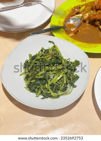 This picture of stir-fried kale is served on a white plate, green plate, spoon, and chocolate background