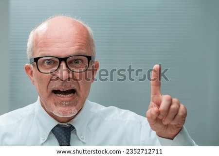 Senior businessman, perhaps pedantic, raises a finger, pointing out oversight. His irritating demeanor and non-macho approach in a male-dominant world hinder his communication, not his expertise Royalty-Free Stock Photo #2352712711
