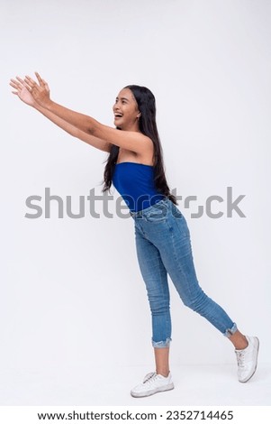 Side view of a young southeast asian woman tries to catch something falling. Reaching out with her arms. Full body photo isolated on a white background. Royalty-Free Stock Photo #2352714465