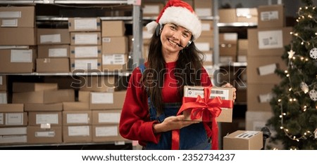Female worker wearing headset and Santa Claus hat in logistics distribution warehouse looking at camera. Banner. Copy space Royalty-Free Stock Photo #2352734237