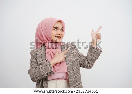 Studio portrait of beautiful young muslim businesswoman pink hijab smiling at camera pointing her finger at empty space on white background