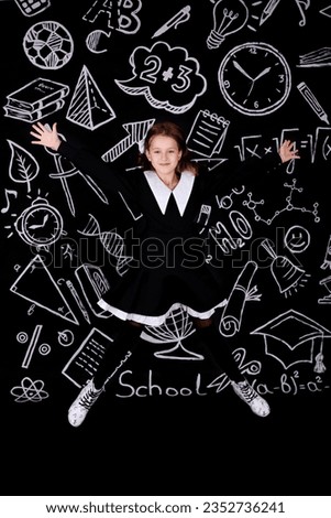 Happy little schoolgirl jumping in the classroom at the blackboard on September 1st. The girl is happy to go back to school. She also celebrates the start of school holidays. Royalty-Free Stock Photo #2352736241