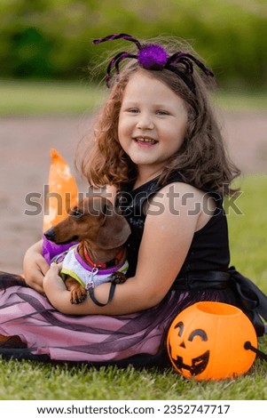 cute little girl in a witch costume for Halloween walks with a dachshund dog in the park. High quality photo