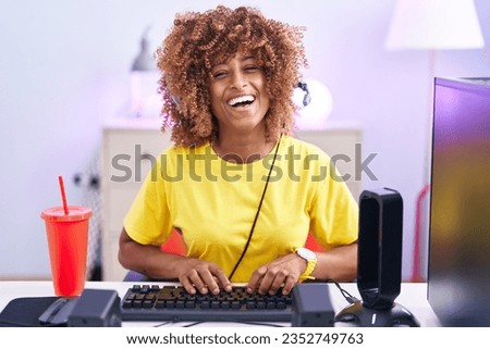 Young hispanic woman with curly hair playing video games wearing headphones with a happy and cool smile on face. lucky person. 