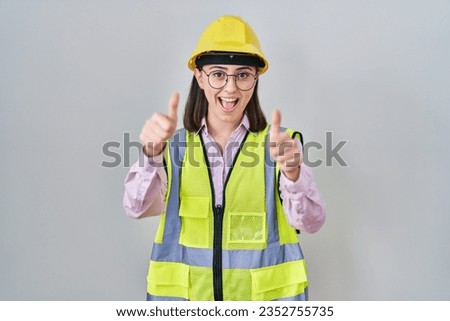 Hispanic girl wearing builder uniform and hardhat approving doing positive gesture with hand, thumbs up smiling and happy for success. winner gesture. 