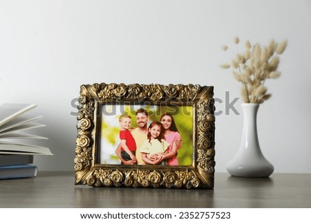 Vintage square frame with family photo, books and vase of dry flowers on wooden table