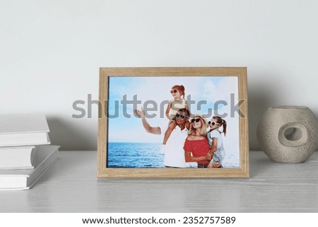 Frame with family photo, books and other decor element on white wooden table indoors