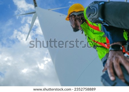 African man workers engineering sitting with confidence with blue working suit dress and safety helmet in front of wind turbine. Concept of smart industry worker operating of renewable energy.