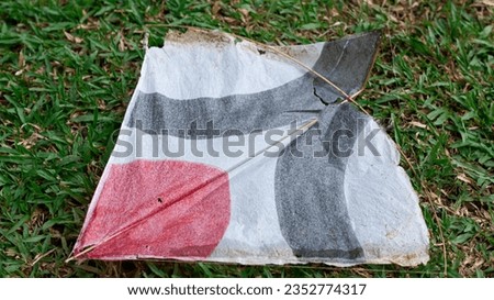 colorful child kites falling on green grass with broken bamboo frame