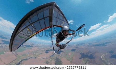 Hang glider pilot on the rainbow colored wing soars high in the sky Royalty-Free Stock Photo #2352776811