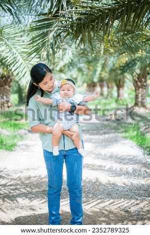 asian woman holding a baby,mother with her child,Asian young beautiful mother holding her newborn is sleeping and feel with love and touching gently then sitting on green grass in the park 