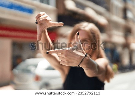 Young blonde woman doing frame gesture with hands at street