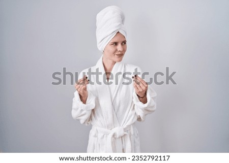 Blonde caucasian woman wearing bathrobe doing money gesture with hands, asking for salary payment, millionaire business 