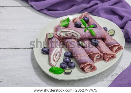 Thin purple pancakes with cream and blueberries. Healthy vegan non lactose and gluten free food, breakfast concept. Trendy hard light, dark shadow, white wooden background, copy space