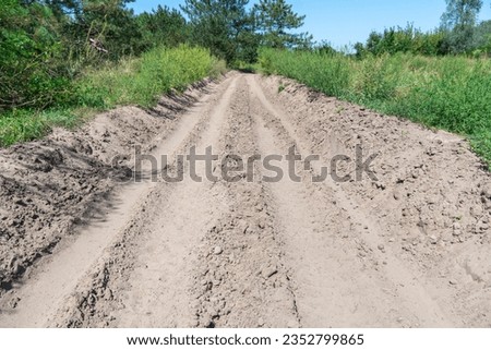 Sand road in the forest. Tire pattern of quad bike on driveway. Track imprint of quadricycle on nature land. Sand texture off road. Path in forest close up. Sand mounds and green forest in sunny day. Royalty-Free Stock Photo #2352799865