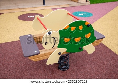 Rocking chair on a green and white metal spring made of natural wood in the shape of a turtle on a playground on a clear sunny day. Children sports hobbies