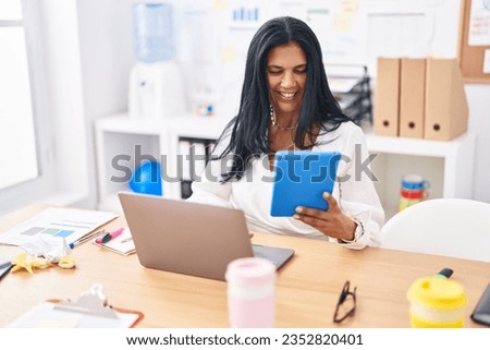 Middle age hispanic woman business worker using touchpad and laptop at office
