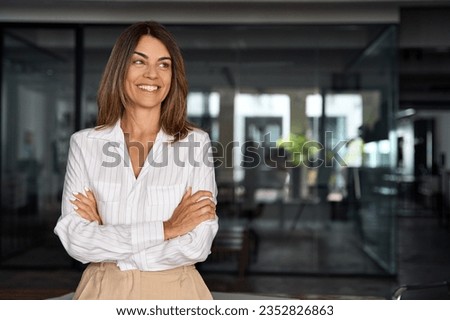 Beautiful hispanic senior business woman with crossed arms smiling, looking aside. European Latin confident mature good looking middle age leader female businesswoman on office background, copy space. Royalty-Free Stock Photo #2352826863