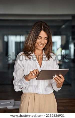 Latin Hispanic 40s years stylish mature professional business woman, smiling European businesswoman CEO holding digital tablet using fintech tab online application standing in modern office, vertical Royalty-Free Stock Photo #2352826931