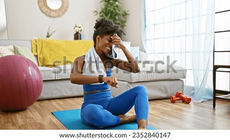 African american woman wearing sportswear looking watch sweating at home Royalty-Free Stock Photo #2352840147