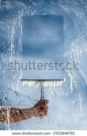 Window cleaner using a squeegee to wash a window with clear blue sky background Royalty-Free Stock Photo #2352848781
