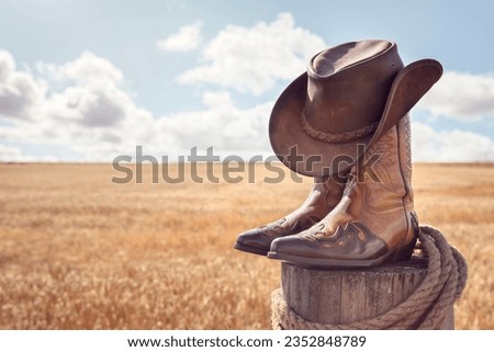 Country music festival live concert with cowboy hat and boots by wheat field at ranch stables background Royalty-Free Stock Photo #2352848789
