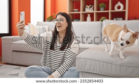 Young hispanic woman with chihuahua dog sitting on the floor taking selfie together at home