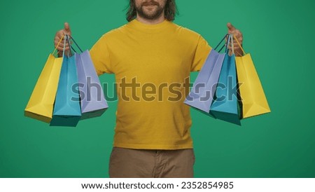 Closeup shot. Delivery man in yellow uniform holding colorful paper bags in hands. Isolated on green background.