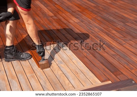 Oiling wooden balcony terrace with a brush, wood deck staining Royalty-Free Stock Photo #2352865107
