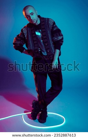 Studio shot of a young tattoed bald man posing against a colorful background. 90s style.