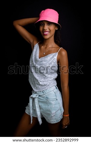 Beautiful teen girl posing for photo in studio. Wearing a pink hat. Isolated on black background.