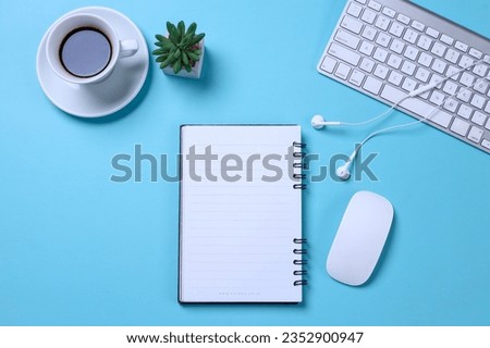 Modern style of blue office desk with blank notebook, keyboard, earphones, computer mouse, succulent and coffee cup. Top view with copy space. 
