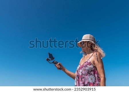 Low angle view of a woman recording with a mobile outdoors with the blue sky in the background