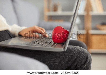 Close up photo of red heart shaped gift box with a engagement ring or jewelry on a laptop computer keyboard on the knees of a man. Proposing, valentines day or online gift and presents concept.