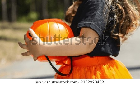 background with child dressed in festive costume for Halloween trick or treating. kid in orange black striped stocking holding pumpkin basket, back view low section