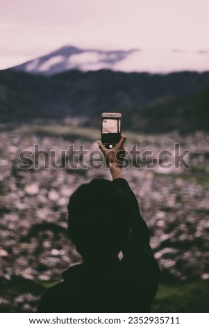 Portrait of person photographing city scape in mountain landscape with smartphone in hand.