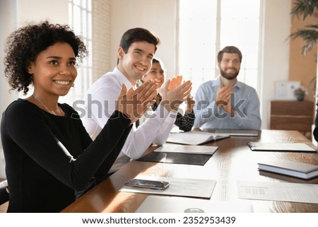 Smiling diverse employees sit at desk applaud greeting trainer or speaker at meeting in office, overjoyed multiethnic colleagues clap hands thanking coach for briefing, acknowledgement concept Royalty-Free Stock Photo #2352953439