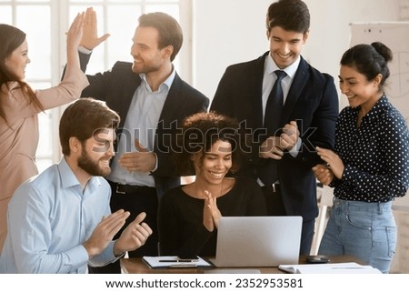 Overjoyed multiracial businesspeople look at laptop screen celebrate shared team business victory cooperating together, happy diverse colleagues work on computer, excited with good results or win