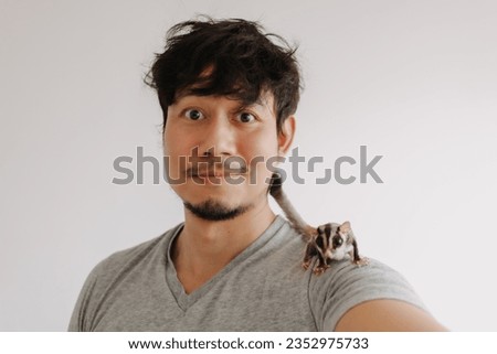 Close up of happy asian man with his Sugar Glider pet climbing around his head.
