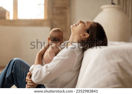Tired young mother suffering from experiencing postnatal depression, sitting on floor and holding newborn baby on hands. Single mom, motherhood stressful Royalty-Free Stock Photo #2352983841