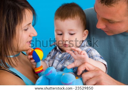 Portrait of happy casual family. Baby boy ( 1 year old ) and young parents father and mother together against blue background, smiling.