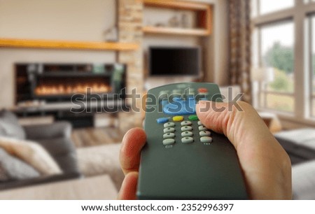 a person hand use a remote control. furnished living room in luxury home with roaring fireplace. modern technology photography..