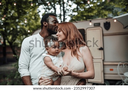 Mixed race family with dark skinned infant daughter spend time together hugs and kisses in camper park. African american man his fair skin wife and little girl enjoying summer vacation in open air
