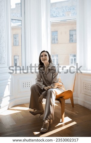 Stylish and elegant brunette sitting by the window, portrait in the interior,sunlight
