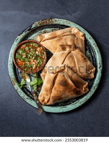 Tipical baked empanadas de pino with pebre sauce on vintage try, black stone background. Traditional chilean food for independence day party Royalty-Free Stock Photo #2353003819