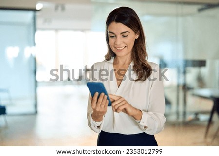 Mid aged mature happy professional business woman using mobile applications on phone at work standing at lobby, businesswoman entrepreneur holding smartphone reading messages on cellphone in office.