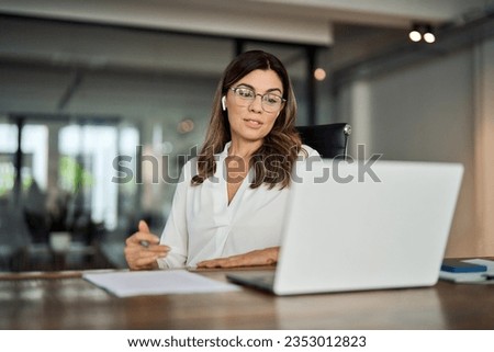 Mid aged business woman having hybrid meeting working in office. Busy mature female corporate leader executive, hr manager communicating by conference call, remote online job interview on laptop. Royalty-Free Stock Photo #2353012823