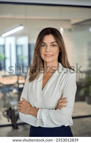 Smiling confident Latin professional mid aged business woman in 40s, corporate leader, happy mature female executive, lady manager standing in office arms crossed looking at camera, vertical portrait. Royalty-Free Stock Photo #2353012839