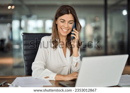 Happy smiling mature middle aged business woman, 40s professional lady executive manager talking on the phone making business call on cellphone at work in office using laptop computer. Royalty-Free Stock Photo #2353012867