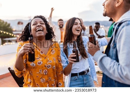 Young group of people dancing together at rooftop party. Diverse friends having fun drinking beer while celebrating birthday at home terrace.